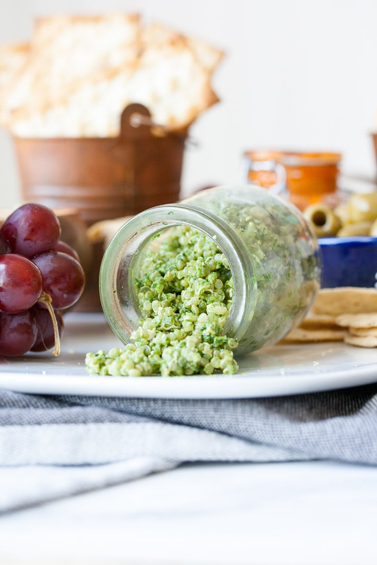 An easy dip made with pesto and quinoa in a jar tipped over on a plate with a cheese platter