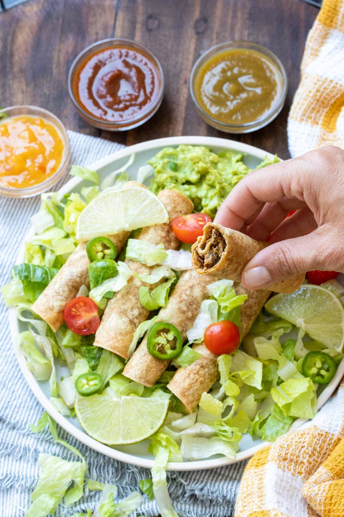 Hand holding a half eaten taquito over a plate of taquitos on a bed of lettuce