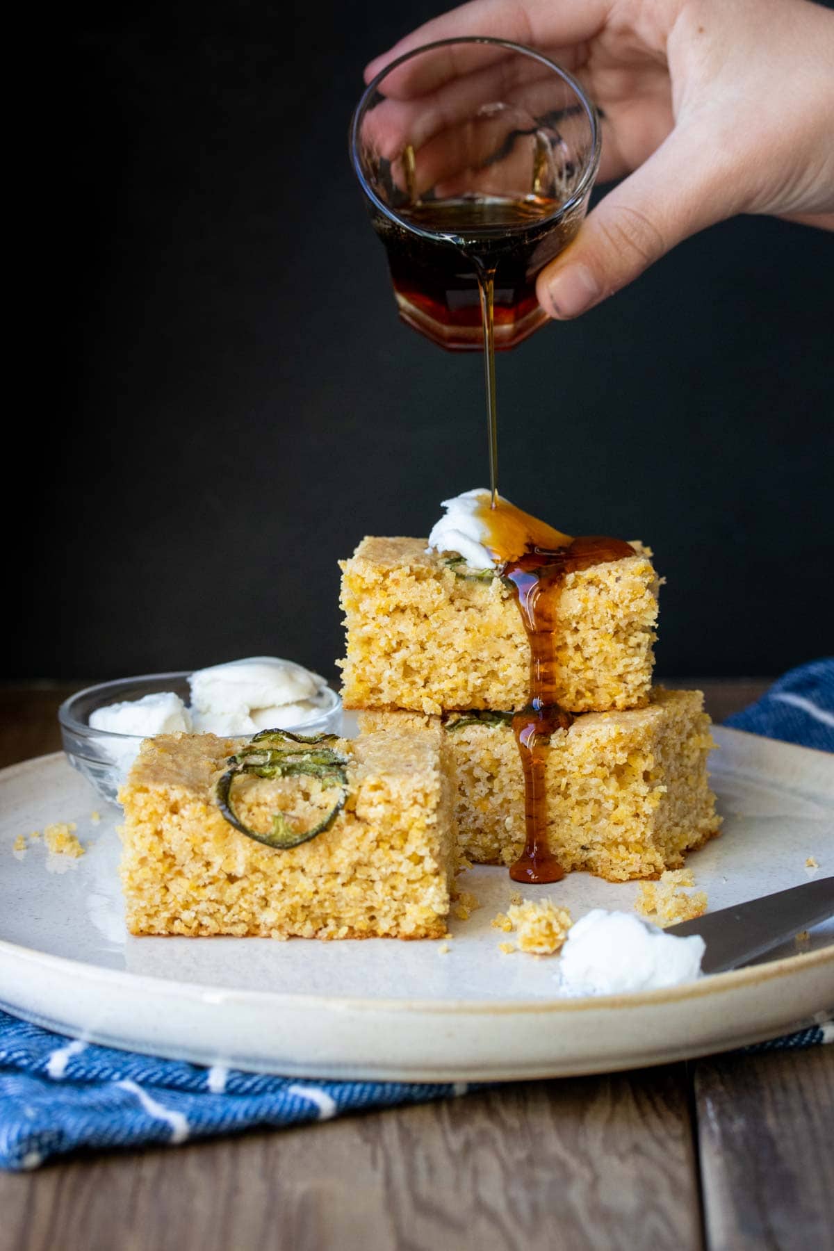 Hand pouring maple syrup on a stack of pieces of cornbread