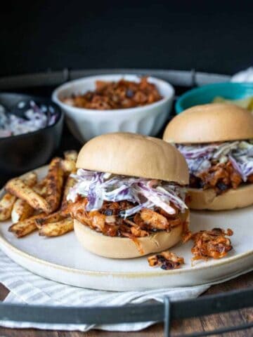 Side view of BBQ jackfruit topped with coleslaw on a bun sitting on a cream plate.