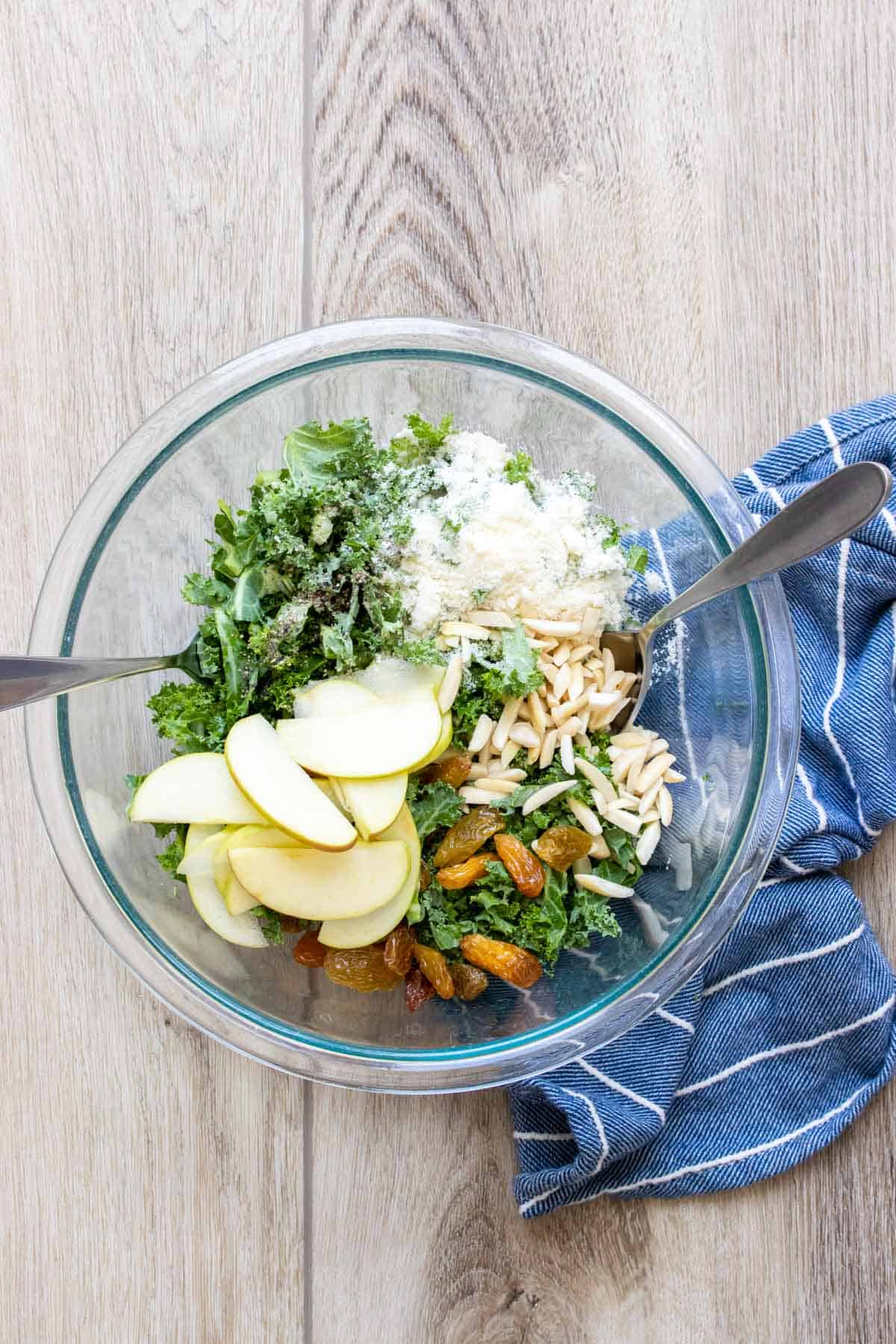 A glass bowl with kale, apples, nuts and Parmesan before being mixed.