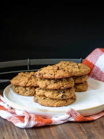 A white plate with a pile of chocolate chip cookies sitting on a checkered orange towel