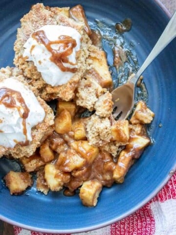 Blue plate with apple cobbler covered by whipped cream and a fork in it