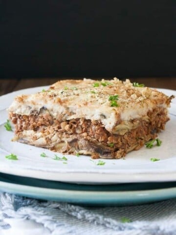 A white plate on top of a blue plate with a piece of moussaka on it.