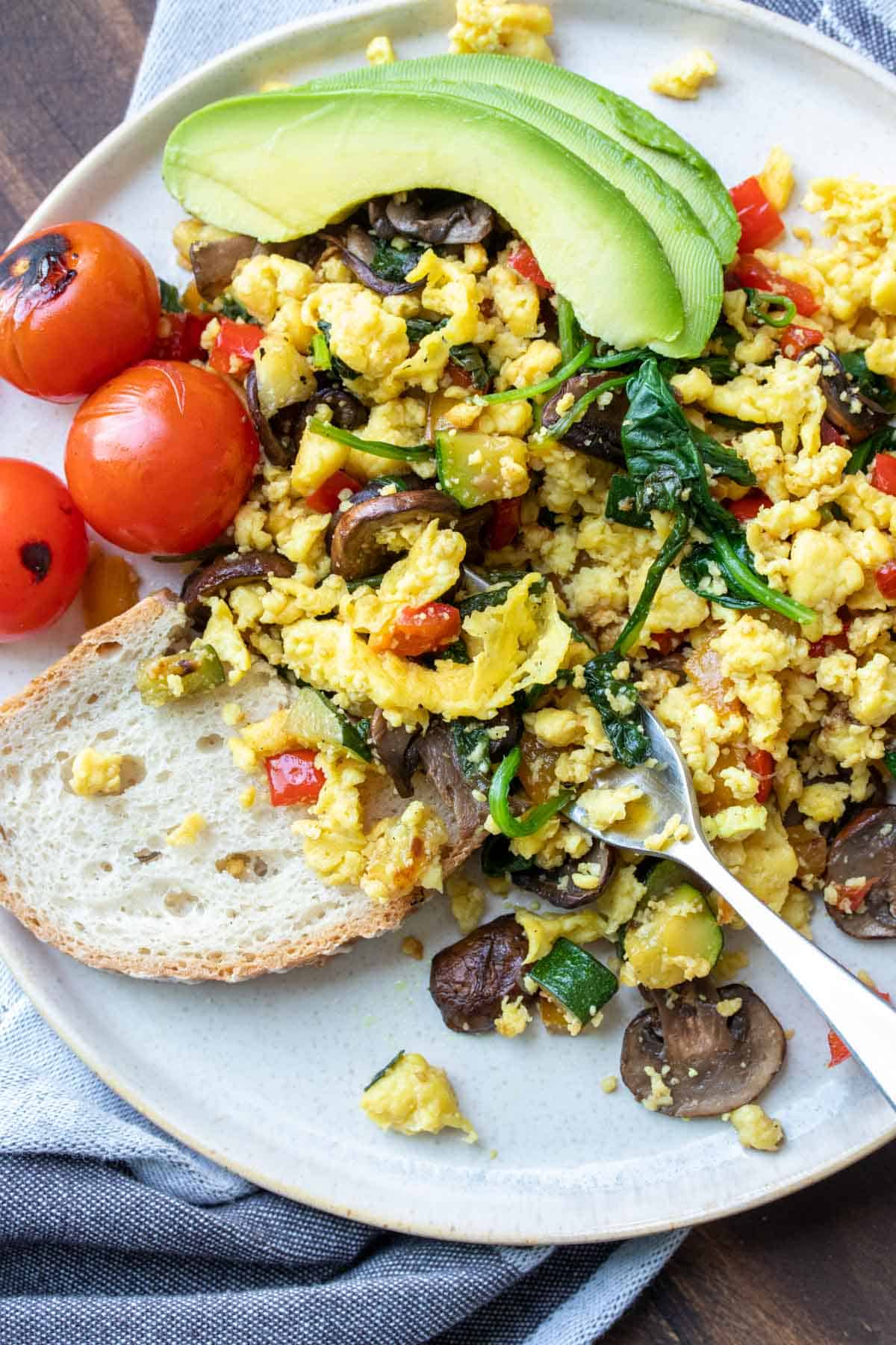 Fork getting a bite of scrambled eggs with veggies from a grey plate