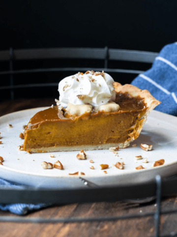 Slice of pumpkin pie on a white plate garnished with nuts and whipped cream