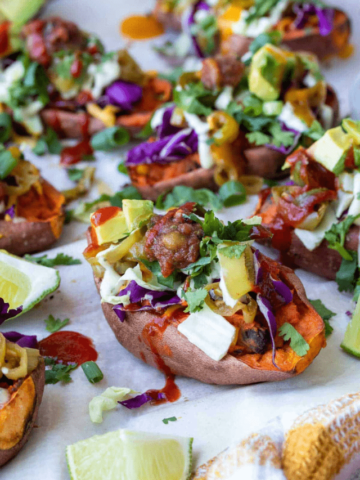 A stuffed sweet potato loaded with toppings sitting on a parchment piece next to others.