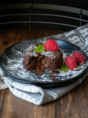 Black plate with a round piece of lava cake and a bite out of it with powdered sugar and raspberries.