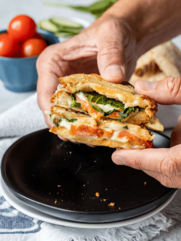 Hands holding a veggie panini cut in half over a plate