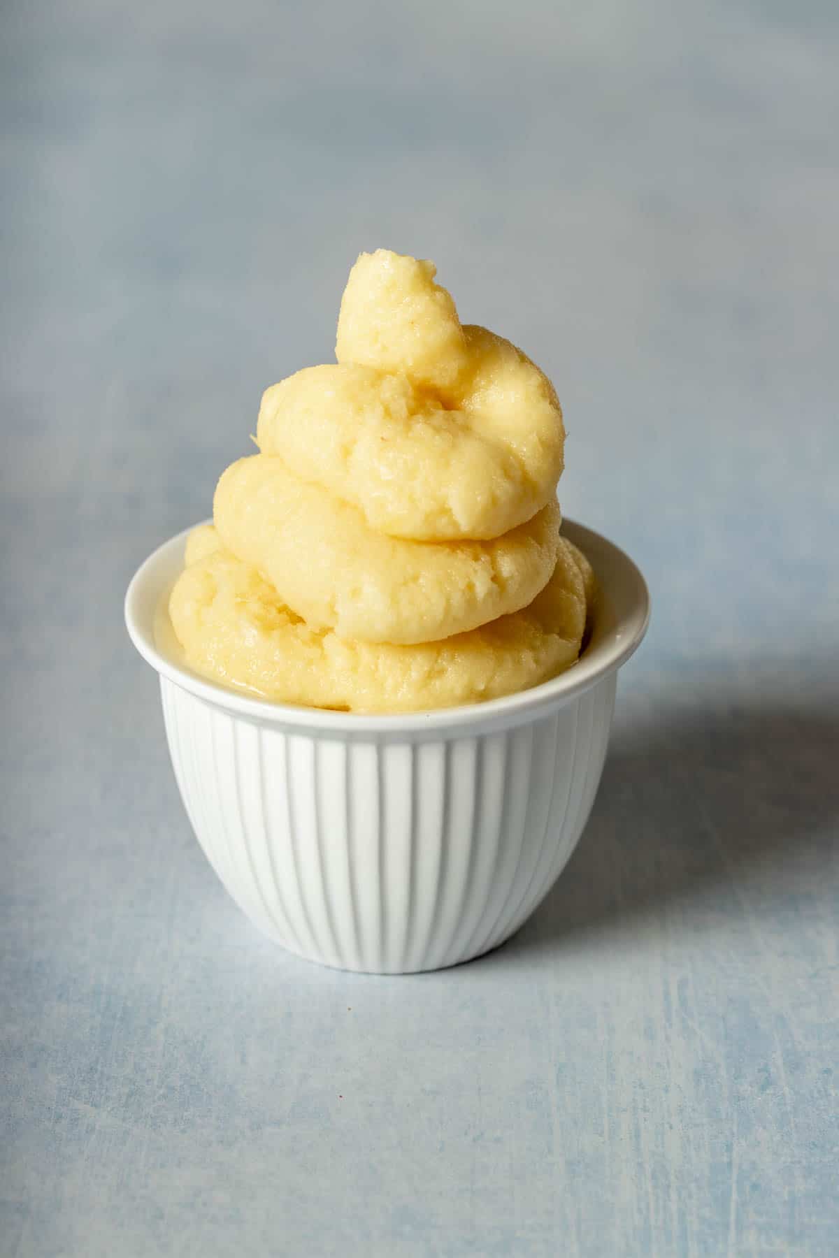 A white textured bowl with dole ship inside piled up high on a blue textured surface.